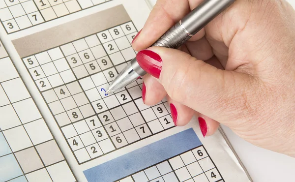 Bir kadının eli kalemle sudoku dolduruyor.