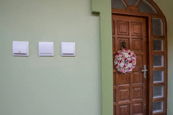 Wooden entrance door with wreath on a  house. Electric switches on a wall