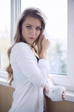 hafif bir arka planda beyaz gömlek ve üst pencerede yakınındaki bir fincan güzel kızla