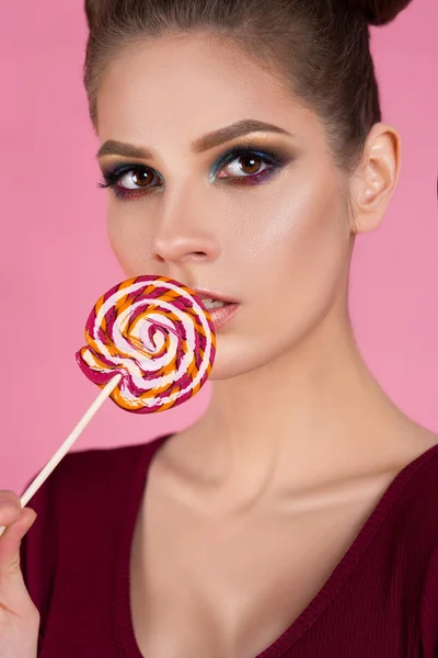 güzel kız bir sopa izole bir pembe arka plan üzerinde şeker yiyor. reklam için bir pudra Dükkanı