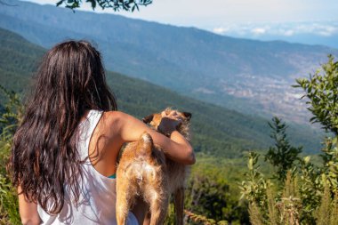 Genç kız köpeğiyle manzaraya bakıyor.