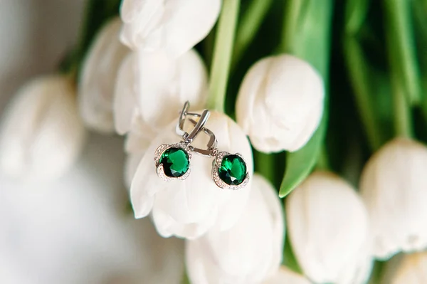 Pair of emerald earrings lying on flowers. White tulips. Jewelry