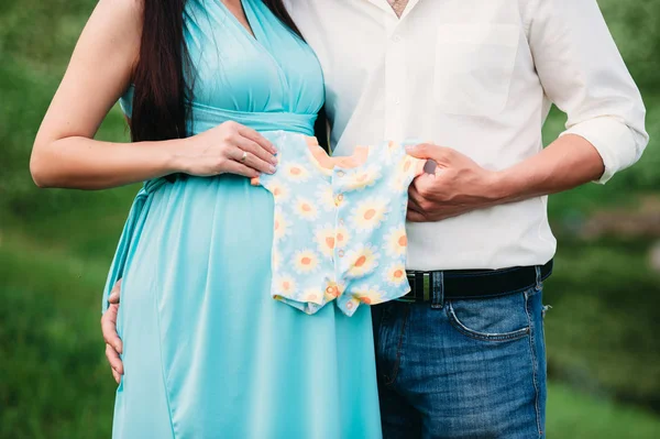 Future paremts holding kids clothes near pregnant belly. Family concept Royalty Free Stock Photos