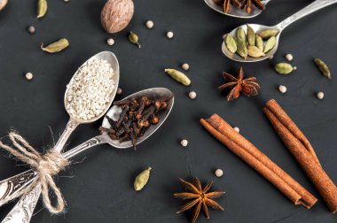 Metal antika kaşık ve tarçın rustik koyu arka plan üzerinde çeşitli baharatlar. Kakule, beyaz biber, küçük hindistan cevizi, anason, karanfil, susam. 