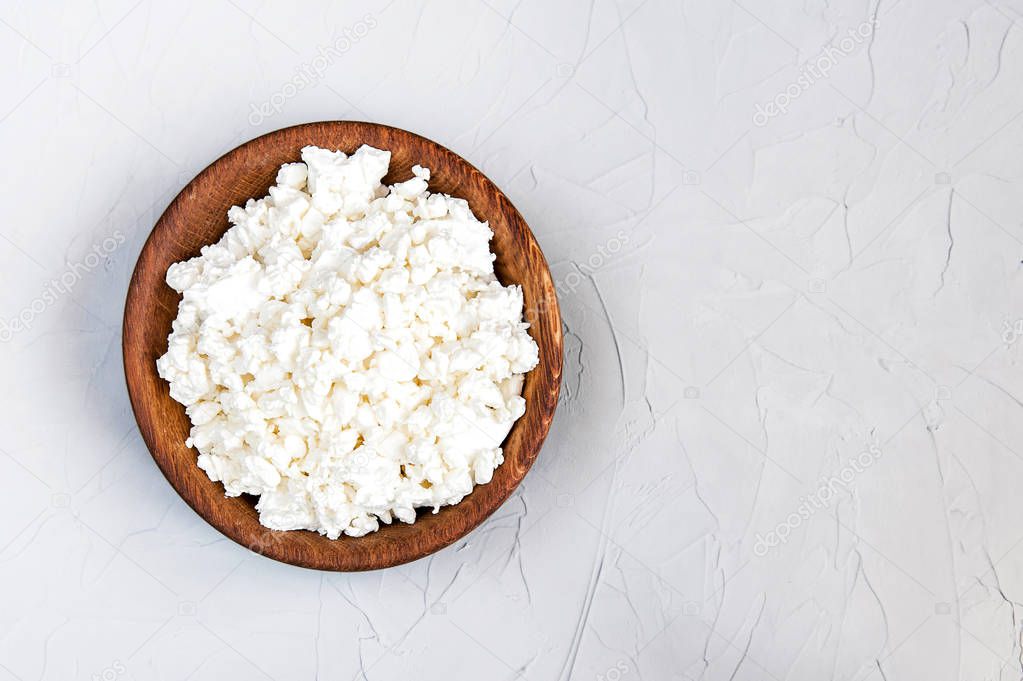 Homemade cottage cheese in a wooden bowl on a grey rustic background.