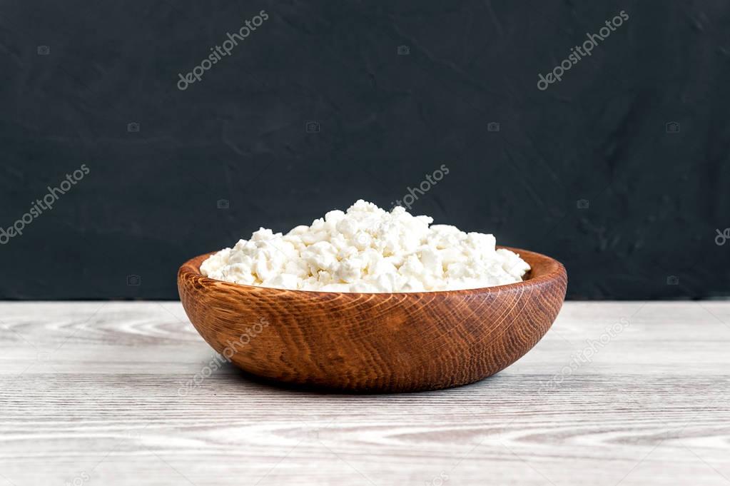 Homemade cottage cheese, curd in a bowl with two crossed spoons on a white rustic wooden table with black background. 