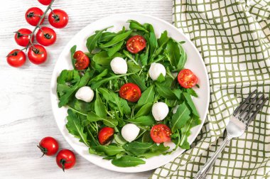 Bahar kiraz domates, mozzarella peyniri ve ahşap masa üzerinde döşeme beyaz tabakta Roka Salatası.