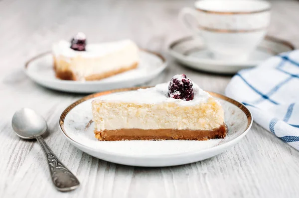 Cheesecake with blackberry on a plate laying on a white wooden table with another cake and cup of coffee or tea on background. delicious breakfast or dessert for two. Stock Picture