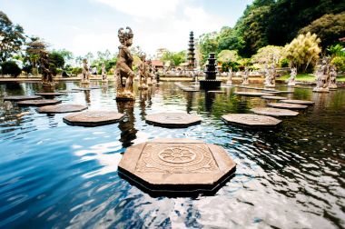 Water Palace Tirta Gangga on Bali island, Indonesia. Labyrinth of decorated stone steps on the water in an artificial lake with statues on a background. Wide angle. clipart