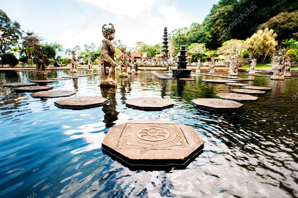 Water Palace Tirta Gangga on Bali island, Indonesia. Labyrinth of decorated stone steps on the water in an artificial lake with statues on a background. Wide angle.