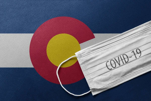 An individual face medical surgical mask on Colorado State Flag Background. Health mask. Protection against COVID-19 virus, influenza, SARS. Coronavirus in Colorado