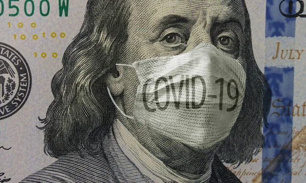 Medical mask with COVID-19 inscription on a banknote of 100 dollars, concept of the global financial crisis. Face surgical mask on american money. Coronavirus in USA. Close up, macro