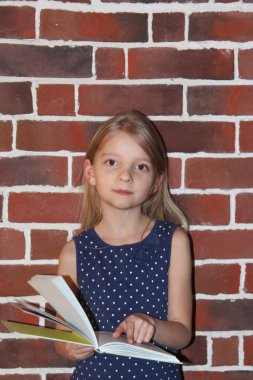 Genç kız ayakta kitap okuyor.