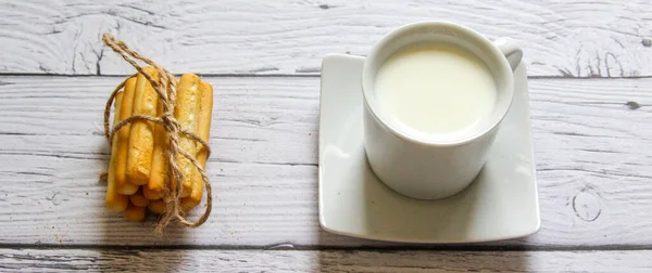 Xícara de leite e breadstick em um fundo de madeira. Café da manhã saudável . — Fotografia de Stock