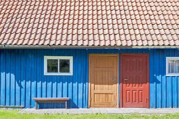 Haus aus blauen Holzbohlen, rotem Dach, zwei bunten Türen und kleinen Fenstern — Stockfoto