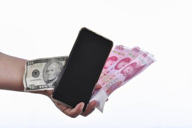 Yuan ve dolar banknotlarının yanında cep telefonu tutan bir el.