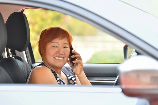 Sonriendo mujer asiática mira a la cámara y habla en el teléfono móvil mientras conduce — Foto de Stock