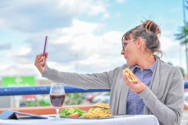 Kadın hamburger yerken selfie çekiyor.