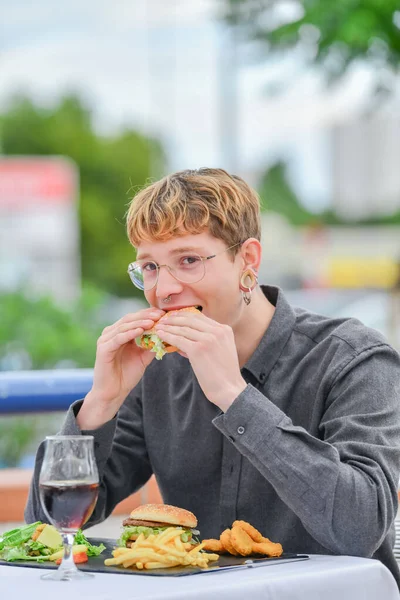 Jovem comendo hambúrguer no restaurante de rua — Fotografia de Stock