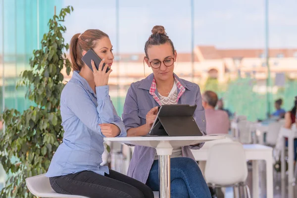 Two woman talking on phone and using tablet computer