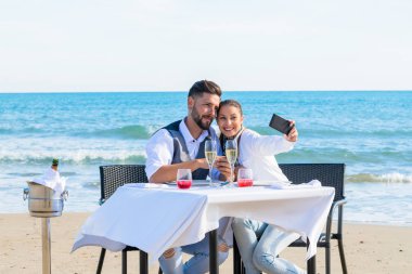 Çiftler sahilde selfie çekerler.