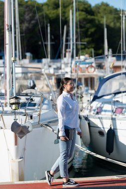 Elinde kitap tutan bir kadın rıhtımda geziniyor.