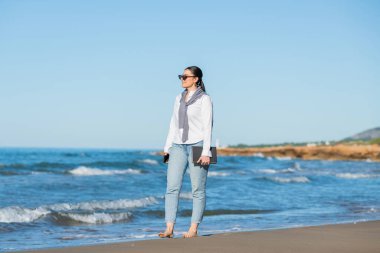 Kadın sahilde yürürken önüne bakar.
