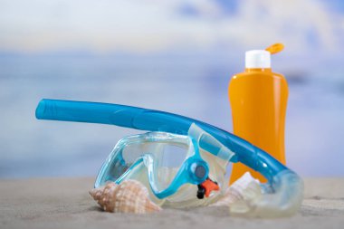 Deniz kabukları ve güneş kremi şişesiyle dalış gözlüğü.