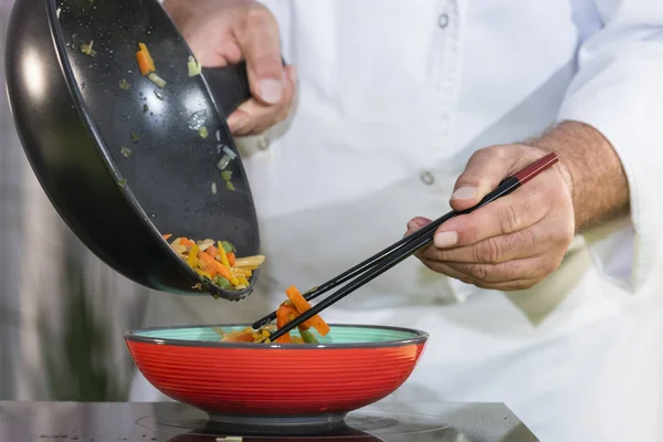 Chef utilise des baguettes pour déplacer les légumes frits dans un bol — Photo