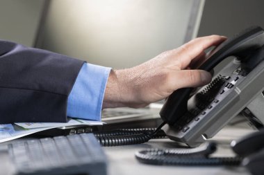 Arka planda odak dışı bir masadaki kablolu telefonu kaldırmak üzere olan bir erkeğin yakın çekimi. İş ve iş kavramı.