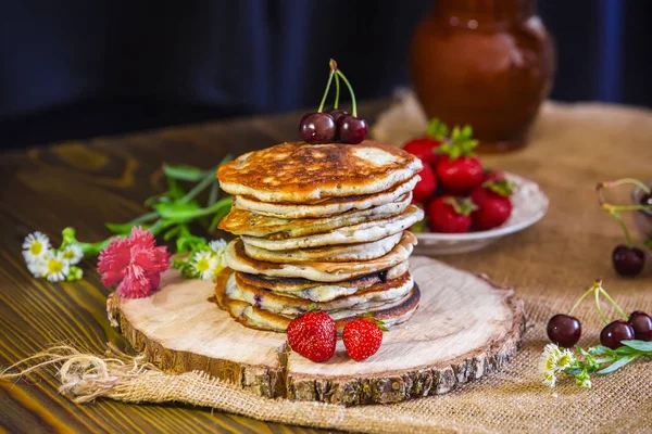 Homemade ruddy pancake with strawberry and cherry on a wooden stand — Stock Photo, Image