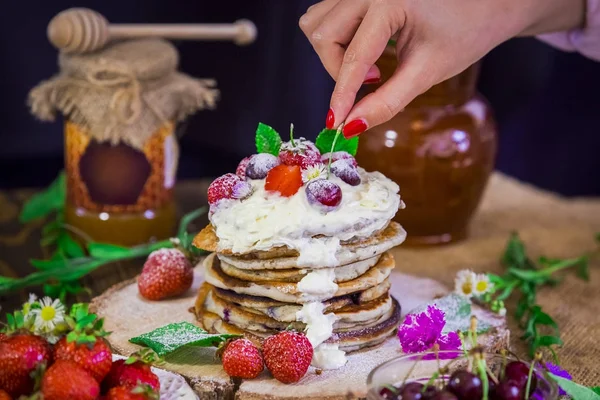 Deliciosas panquecas com bagas no suporte de madeira. Cereja de mão sob panquecas polvilhadas com pó e creme — Fotografia de Stock