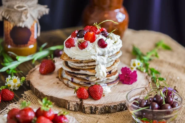 Delicious pancakes with berries on the authentic wooden stand. Summer food still life concept. Pancakes sprinkled with powder and cream
