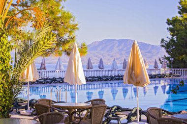 Yüksek katlı konforlu. Boş hotel, Yüzme Havuzu, deniz, palmiye ağaçları, şemsiye, tablolar, güneşlenme yatakları, arka planda dağlar