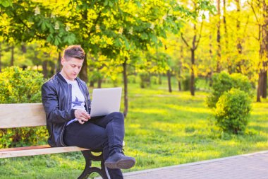 Genç yakışıklı bir adam oturuyor ve parkta bir dizüstü bilgisayar ile çalışma. Adam serbest meslek işleri dışında