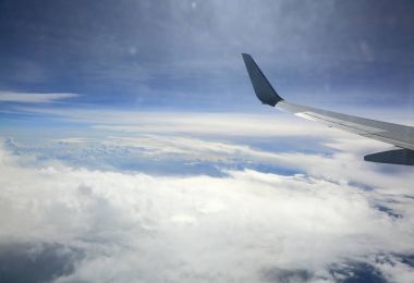 Kabin penceresinden uçak kanat bak. Mavi gökyüzü, beyaz bulutlar ve arazi aşağıda. Güzel arka plan. 