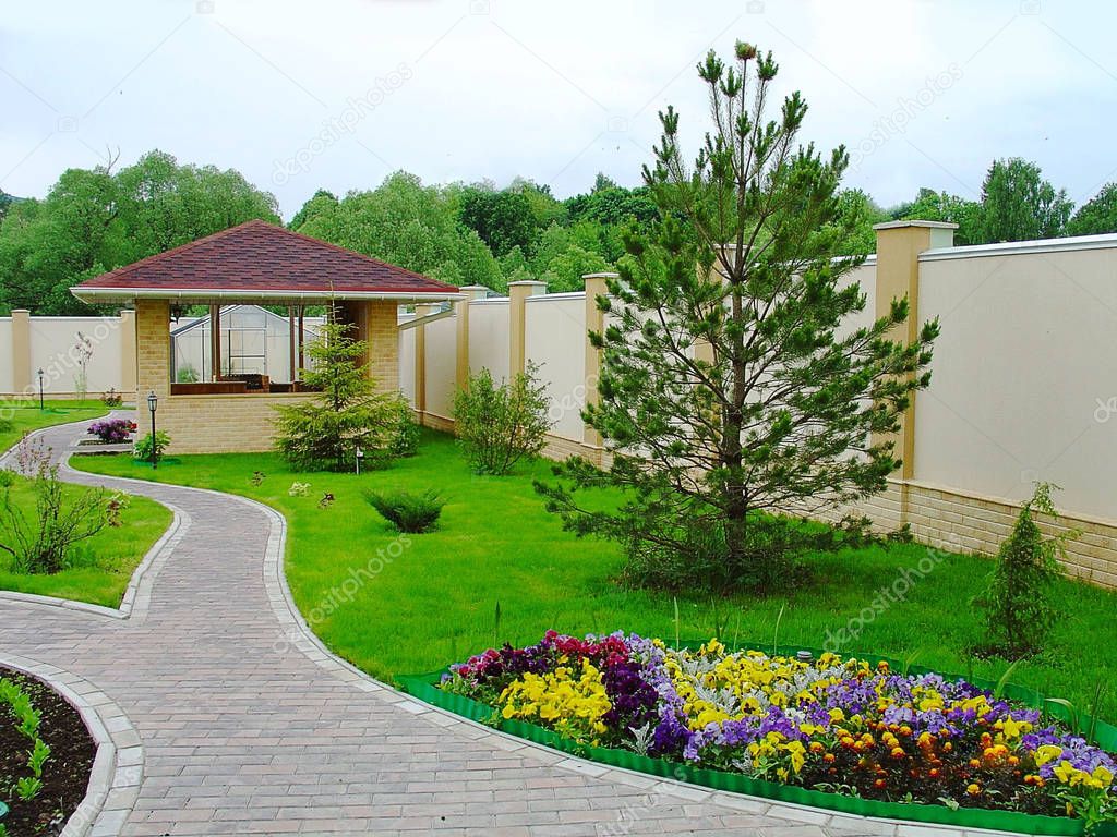 Beautiful landscape design in a private yard. Colorful flowers, green grass and trees. Cosy barbeque house / grill house. Beautiful exterior.