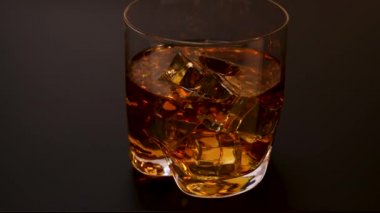 Siyah zemin üzerinde buz küpleri olan yaklaşan viski bardağının güzel manzarası. Alkol konsepti. Yiyecek ve içecekler. 