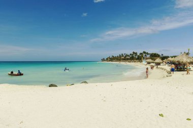 Atlantik Okyanusu 'nda su aktiviteleri yapan turistler. Sörf egzersizi. Turkuaz okyanus suyu yüzeyi mavi gökyüzü ile birleşiyor. Beyaz kumsal ve yeşil palmiye ağaçları. Oranjestad. Aruba. 09.11.2019.