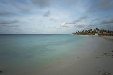 Beyaz kumsal ve turkuaz dalgalar. Turkuaz deniz suyu ve mavi gökyüzü. Aruba Adası 'nın Kartal Sahili. Güzel arka planlar.
