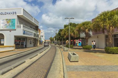 Oranjestad sokaklarından birinin güzel manzarası. Binalar ve yeşil ağaçlar mavi gökyüzü üzerindeki tramvay rayları boyunca beyaz bulutlu arka planlar. Oranjestad. Aruba, 09.13.2019.