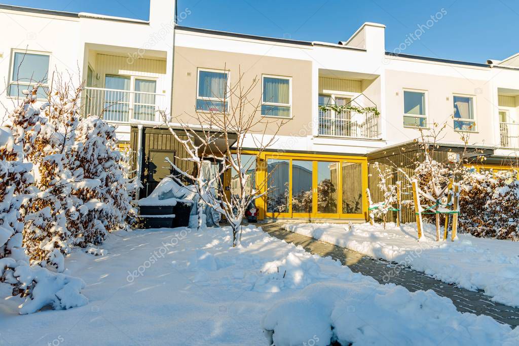 Beautifil exterior view of townhouseswith front yard covered with snow. White and yellow on blue sky background. 