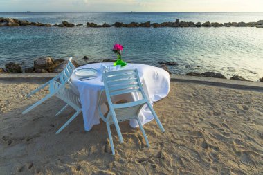 Atlantik Okyanusu kıyısında beyaz bez ve kırmızı çiçeklerle kaplı güzel bir masa manzarası. Romantik bir kavram. Curacao. Willemstad.