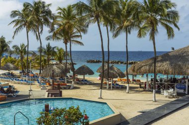 Otel manzarası çok güzel. Açık havuz, mavi güneş yatakları ve yeşil palmiye ağaçları üzerinde şemsiyeler ve kar beyaz bulutlu mavi gökyüzü. Willemstad. Curacao. 09.18.2019.