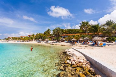 Beyaz Curacao plajının güzel manzarası. Güneş şemsiyelerinin altında mavi güneşlikler turkuaz su ve beyaz bulutlu mavi gökyüzü. Curacao Adası. Willemstad. Curacao. 09.18.2019