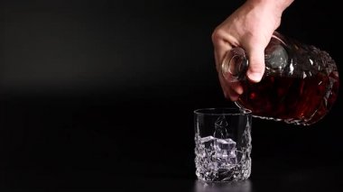 Siyah arka planda buzla bardağa dökülen viskiyi gösteren kısa film. Ağır çekim. Güzel arka planlar. Alkol kavramı.