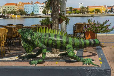 Açık hava restoranının dekorasyonu olarak büyük yeşil iguana figürünün yakın görüntüsü. Saint Anna Körfezi ve arka planda renkli binalar. Willemstad. Curacao. 