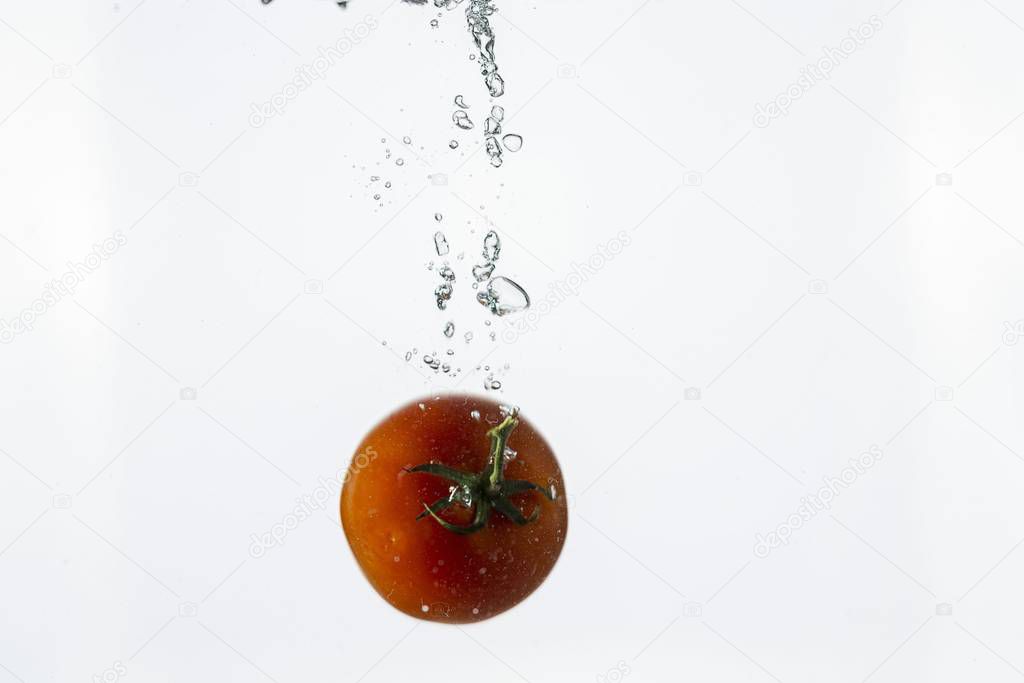 Close up view splashing water and red tomato  on white background. Beautiful backgrounds.