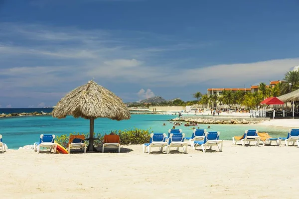 Beyaz Curacao plajının güzel manzarası. Güneş şemsiyelerinin altında mavi güneşlikler turkuaz su ve beyaz bulutlu mavi gökyüzü. Curacao Adası. Willemstad. Curacao. 