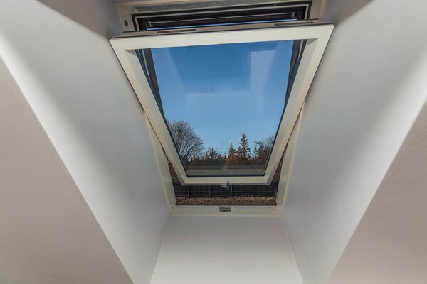 Close up view of open roof window isolated with view of trees on blue sky background.